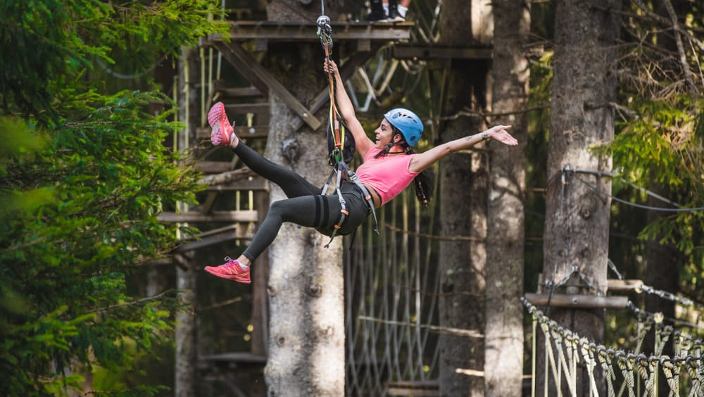 Frau im Hochseilpark schwingt an Seil zwischen Bäumen